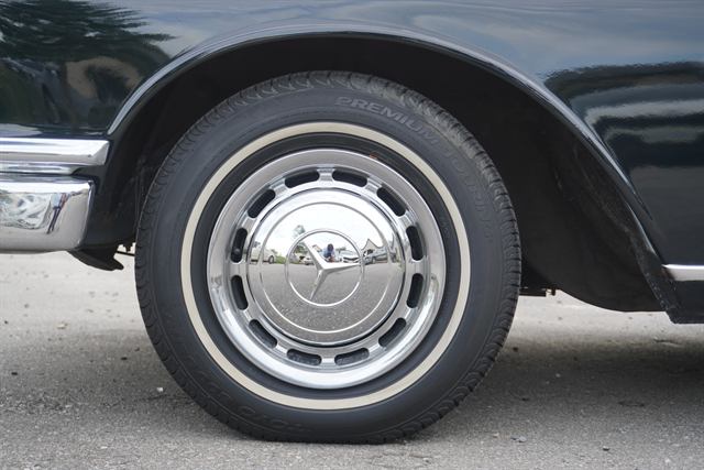 Dressed whitewall tire and polished chrome hubcap on a black Mercedes-Benz.