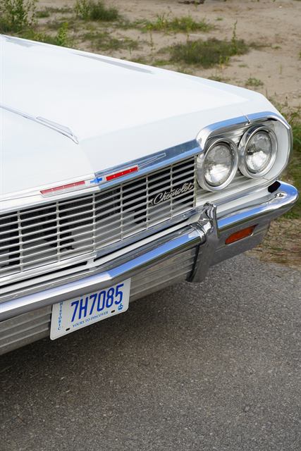 Chrome grille, quad headlights and front bumper of a white Chevrolet Impala.