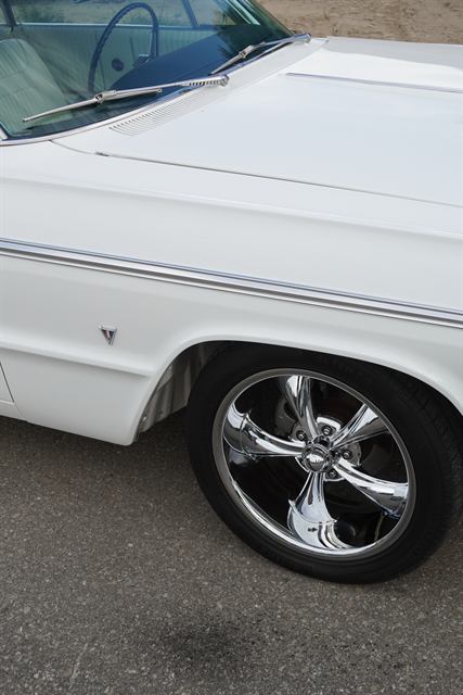 Polished chrome wheel and cleaned front quarter panel of a white Chevrolet Impala.